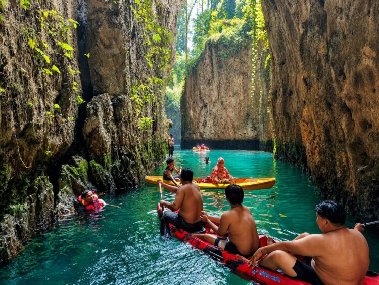 Suasana ramai wisatawan menikmati keindahan Goa Gumantung dengan bermain perahu kano di antara tebing-tebing karst yang menjulang tinggi. Air berwarna hijau kebiruan yang jernih menjadi daya tarik utama destinasi wisata alam di Kampung Teluk Alulu, Kecamatan Maratua, Kabupaten Berau. (Foto: iN/sudutkata.com)